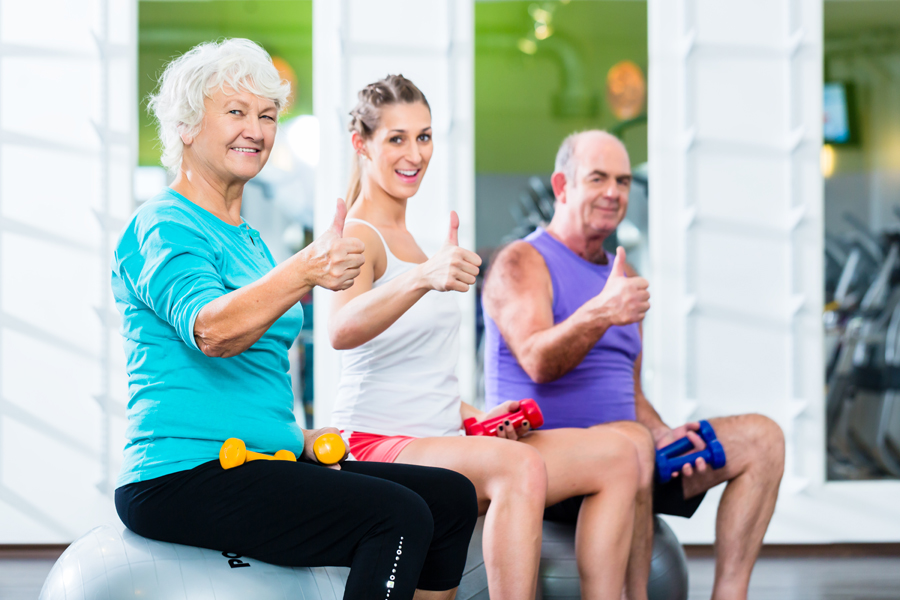 Seniors with trainer in gym at sport lifting barbell