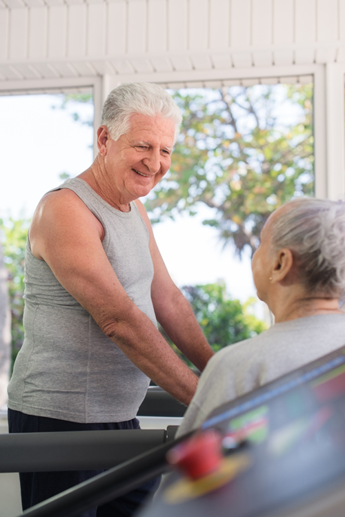 Active retired people, old man and woman talking and exercising in fitness gym