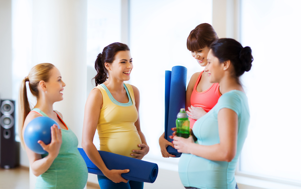 group of happy pregnant women talking in gym